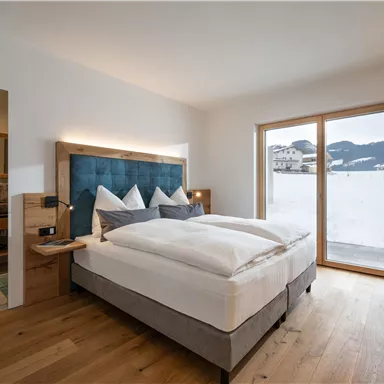 Ein modernes Schlafzimmer mit einem großen Bett und gemütlicher Ausstattung. Große Fenster bieten Blick auf die snowy Landschaft.
