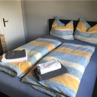 Ein gemütliches Schlafzimmer mit einem Doppelbett und bunten Bettdecken. Auf dem Bett liegen frische Handtücher bereit.