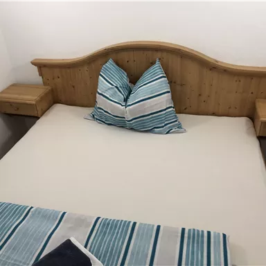 Ein einfaches Schlafzimmer mit einem Holzbett und gestreiften Kissen. Neben dem Bett befinden sich zwei Nachttische.