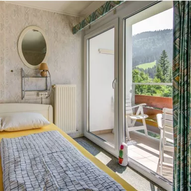 A cozy bedroom with a double bed and a balcony overlooking the mountains. The room features bright, cheerful decor and large windows for plenty of daylight.
