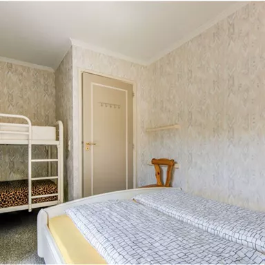 A simple bedroom with a bunk bed and a single bed. The walls are decorated with patterned wallpaper.