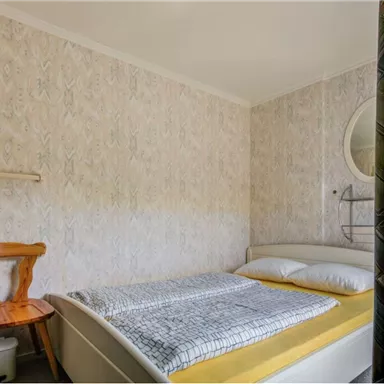 A simple bedroom with a bed, a chair, and bright walls. The decor is modern and minimalist.