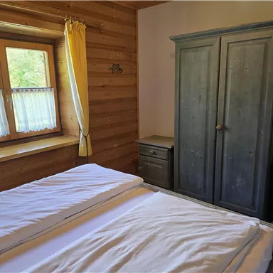 Ein gemütliches Schlafzimmer mit einem großen Fenster und Holzwänden. Es gibt ein Bett ohne Bettwäsche und einen blauen Schrank.