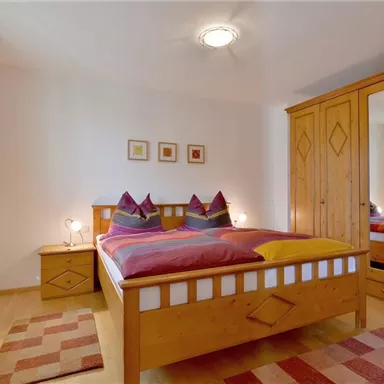Ein gemütliches Schlafzimmer mit einem großen Bett und Holzschränken. Die Wände sind hell und die Fenster lassen viel Licht herein.