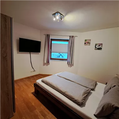 Ein gemütliches Schlafzimmer mit einem Doppelbett und hellen Wänden. Ein Fernseher und ein Fenster sorgen für angenehmes Licht.