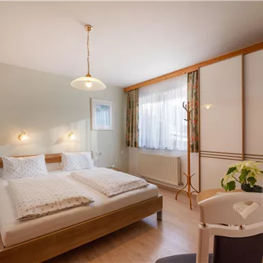 A bright and modern bedroom with a double bed and soft colors. The room is equipped with a window, chairs, and a television.