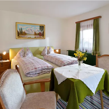 Ein gemütliches Zimmer mit zwei Betten und einem Tisch. Es gibt Stühle und eine schöne Dekoration an den Wänden.