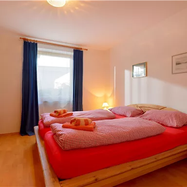 A cozy bedroom with a large bed and colorful pillows. Natural light comes in through the window and the floor is made of wood.