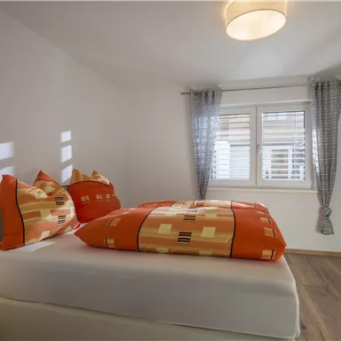 A modern bedroom with a cozy bed and colorful pillows. Large windows provide plenty of natural light.