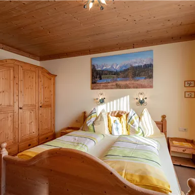 A cozy bedroom with a wooden wardrobe and a large bed. A picture of a mountain landscape hangs on the wall.
