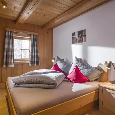 A cozy bedroom with wooden walls and a large bed. The decorative red pillows and the window create an inviting atmosphere.