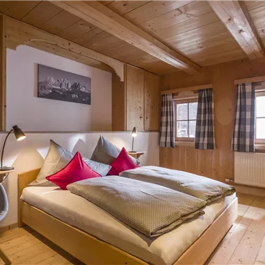 A cozy bedroom with a double bed and colorful cushions. Wood paneling and large windows create a warm atmosphere.