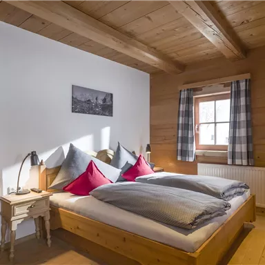 A cozy bedroom with a wooden design. Two beds with red pillows and a window overlooking nature.