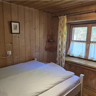 Ein gemütliches Schlafzimmer mit Holzwänden und einem großen Fenster. Das Bett ist mit weißen Bettwäsche ausgestattet und es gibt helle Vorhänge.