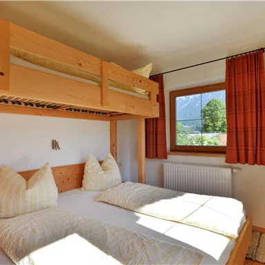 Ein gemütliches Schlafzimmer mit einem Etagenbett und einem Doppelbett. Große Fenster bieten viel Tageslicht und einen Blick ins Freie.