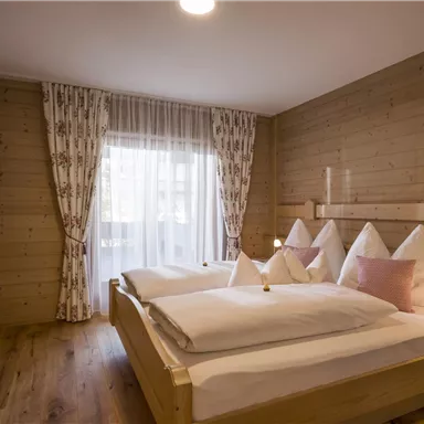 Ein gemütliches Schlafzimmer mit zwei Einzelbetten und Holzverkleidung. Große Fenster mit Vorhängen lassen viel Licht herein.