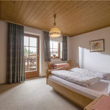 A cozy bedroom with a wooden ceiling and soft colors. The room features a balcony, two beds, and warm lighting.