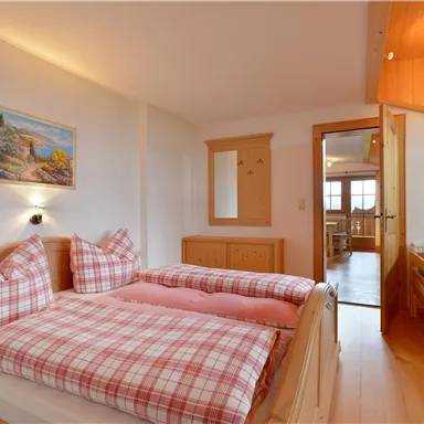 Ein gemütliches Schlafzimmer mit zwei Betten und karierten Bettdecken. Die warmen Holzmöbel und die dezente Dekoration schaffen eine einladende Atmosphäre.