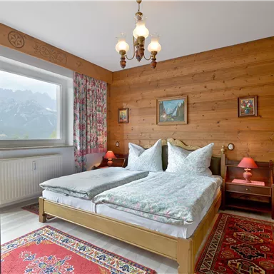 A cozy bedroom with wooden walls and a large bed. The decoration includes colored curtains, a rug, and beautiful pictures on the wall.