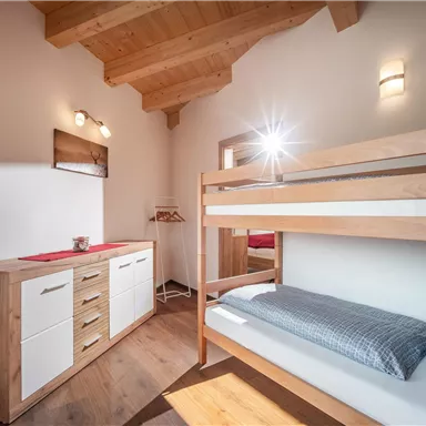 A cozy bedroom with a wooden bunk bed and modern furniture. Large windows provide plenty of light and a warm atmosphere.