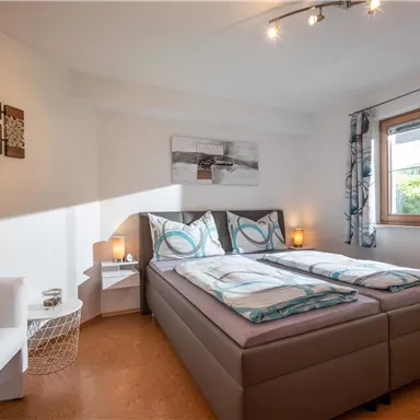 Ein modernes Schlafzimmer mit einem Doppelbett und einem gemütlichen Sessel. Das Zimmer hat große Fenster und eine helle, einladende Atmosphäre.