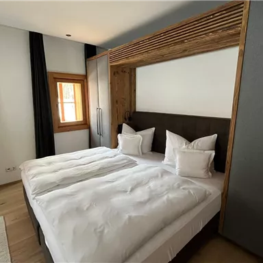 Ein modernes Schlafzimmer mit einem Doppelbett und weißen Betten. Große Fenster mit schwarzen Vorhängen bieten Licht und Atmosphäre.