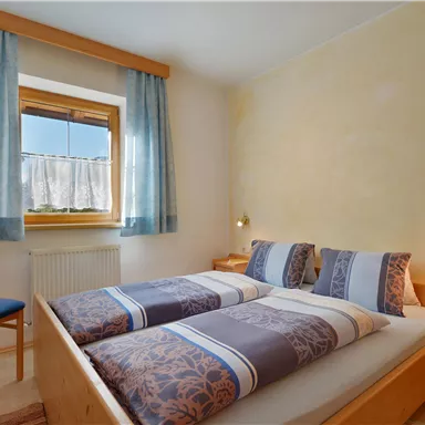 Ein gemütliches Schlafzimmer mit zwei Betten und hellen Wänden. Das Fenster lässt viel Licht herein, und die blauen Vorhänge ergänzen die warme Atmosphäre.