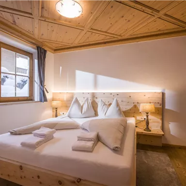 Ein gemütliches Schlafzimmer mit einem Doppelbett und modernen Holzmöbeln. Durch das Fenster fällt natürliches Licht und zeigt eine verschneite Landschaft draußen.