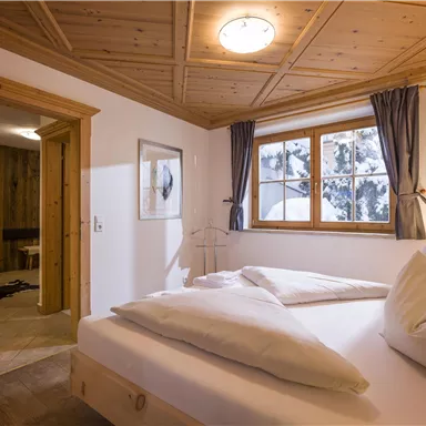 Ein gemütliches Schlafzimmer mit Holzmöbeln. Große Fenster bieten einen Blick auf die verschneite Landschaft draußen.