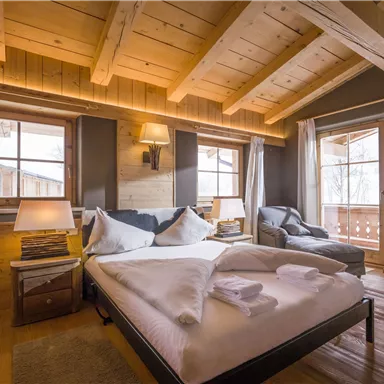 Ein gemütliches Schlafzimmer mit Holzbalkendecke und großen Fenstern. Das Zimmer ist geschmackvoll eingerichtet und bietet eine entspannte Atmosphäre.