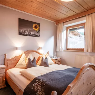 A cozy bedroom with a wooden double bed. Soft colors and a window create a bright, inviting atmosphere.