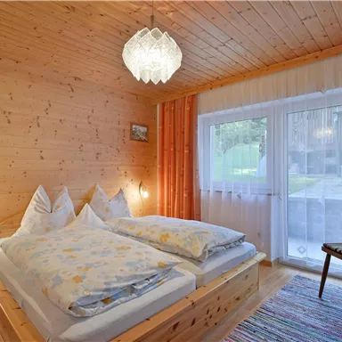 Ein gemütliches Schlafzimmer mit Holzverkleidung und zwei Betten. Es gibt einen Stuhl und große Fenster, die viel Licht hereinlassen.
