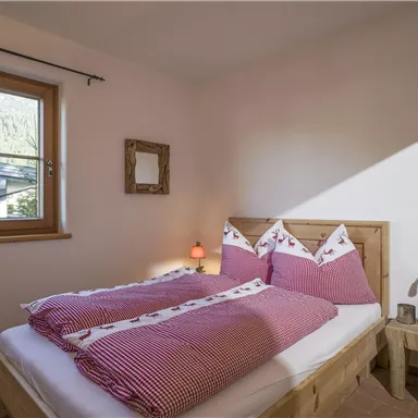 A cozy bedroom with a wooden bed and purple checked bedding. A window lets in natural light, creating an inviting atmosphere.