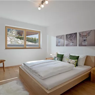 Ein gemütliches Schlafzimmer mit einem Bett und zwei Nachttischen. An der Wand hängen dekorative Bilder von Rehen und ein Fenster lässt viel Tageslicht herein.