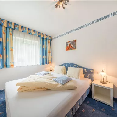 A cozy bedroom with a large bed and colorful curtains. It has a bright atmosphere and a small bedside table next to the bed.