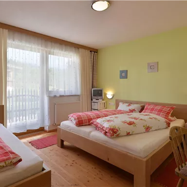 Ein gemütliches Schlafzimmer mit zwei Betten und hellen Farben. Große Fenster sorgen für viel Tageslicht.