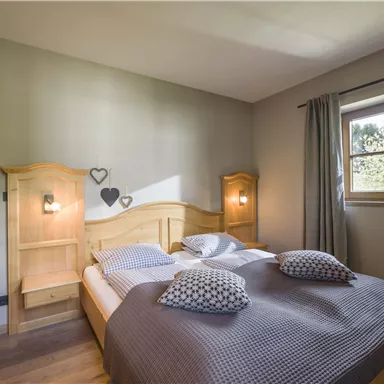 Ein gemütliches Schlafzimmer mit einem Doppelbett und natürlichen Holzdetails. Das Zimmer hat Fenster mit Vorhängen und eine warme, einladende Atmosphäre.
