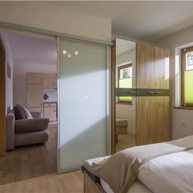 Ein modernes und helles Schlafzimmer mit einem Doppelbett und Holzfußboden. Im Hintergrund ist ein gemütlicher Aufenthaltsbereich sichtbar.