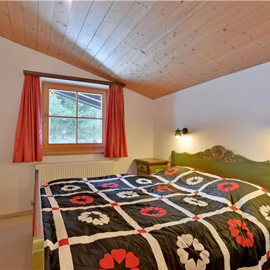 Ein gemütliches Schlafzimmer mit einem großen Bett und buntem Bettzeug. Die Wände sind hell und das Zimmer hat ein Fenster mit Blick ins Freie.