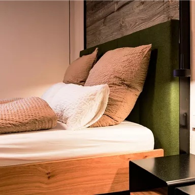 A modern bedroom with a cozy bed and two pillows. Next to the bed is a black nightstand.