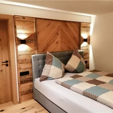 A modern bedroom with a cozy bed and a wooden wall. The decoration is simple and inviting.