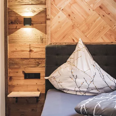 A modern bedroom with a wooden wall design. The bed is equipped with decorative pillows and has a stylish bedside lamp.