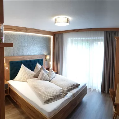 Ein gemütliches Schlafzimmer mit einem großen Bett und hellen Vorhängen. Der Raum hat Holzdetails und einen Schreibtisch.