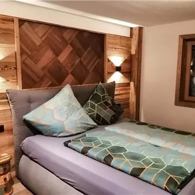 A cozy bedroom with an elegant bed and wood paneling. The pillows and duvet are designed in pleasing colors.