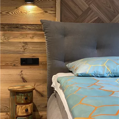 A cozy bedroom with a large bed and an interesting wooden wall. Next to the bed is a colorful nightstand with several drawers.