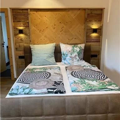 A comfortable double bed with colorful blankets and pillows. The head area is made of wood and is illuminated by modern wall lamps.