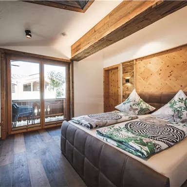 A cozy bedroom with two beds and colorful cushions. Large windows provide a view of a balcony and let in plenty of light.