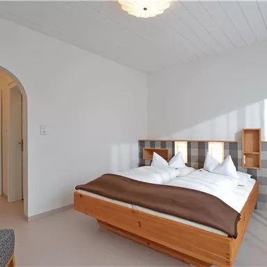 Ein einfaches, modernes Schlafzimmer mit einem großen Bett und weißen Bettwäsche. Der Raum ist hell erleuchtet und hat einen minimalistischen Stil.