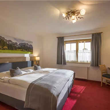 Ein gemütliches Schlafzimmer mit einem großen Bett und einem modernen Holzdesign. Die Wände sind hell, und ein schönes Bild der Berge hängt über dem Bett.