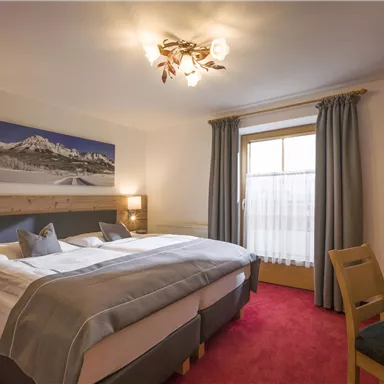 Ein helles Hotelzimmer mit zwei Betten und einem gemütlichen Ambiente. Das Zimmer ist mit einem Tisch und einem Fenster mit Blick nach draußen ausgestattet.